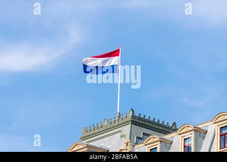 Drapeau du Royaume des Pays-Bas en bandes rouges, blanches et bleues de tissu attaché à un flagpole sur un bâtiment et soufflant dans le vent. Banque D'Images