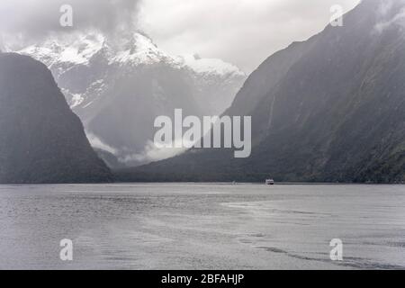 Paysage avec bateaux à passagers naviguant parmi les côtes vertes abruptes et pics avec neige sur le fjord, tourné en lumière vive à Milford Sound, Southland, S Banque D'Images