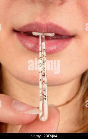 Une femme avec un thermomètre au mercure dans sa bouche. Elle prend sa propre température pour diagnostiquer les symptômes de la grippe (grippe). Elle utilise un Banque D'Images