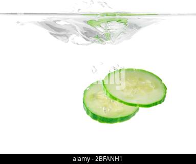 Chute de tranches de concombre frais dans l'eau sur fond blanc Banque D'Images