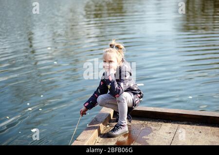 Enfant gai dans un jaket bleu se posant à l'extérieur. La jeune fille caucasienne bénéficie d'un style de vie lumineux de printemps Banque D'Images