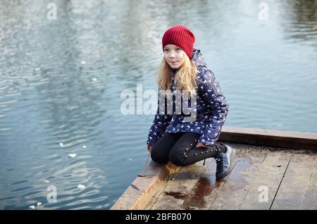 Enfant gai dans un jaket bleu se posant à l'extérieur. La jeune fille caucasienne bénéficie d'un style de vie lumineux de printemps Banque D'Images