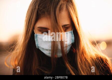 Gros plan portrait de triste jeune femme déprimée portant un masque médical protecteur du visage en se tenant en ville pendant le coucher du soleil
