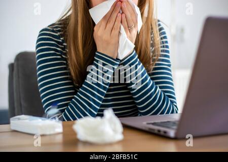 Femme malade travaillant sur ordinateur portable à la maison, couvrant le nez et la bouche lors de la toux et des éternuements dans le tissu de papier, femme pigiste malade avec travail à froid Banque D'Images