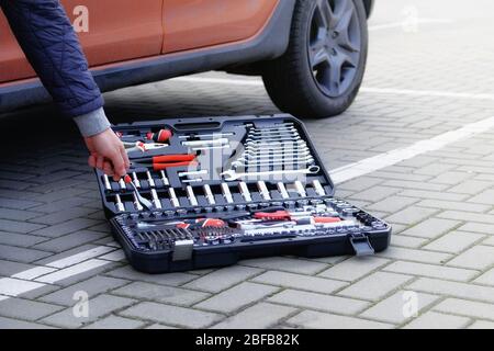 Boîte à outils mécaniques. Сar conducteur utilisant différents outils de réparation pour réparer et entretenir une voiture orange. Jeu d'outils près de l'auto. Gros plan. Banque D'Images