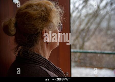 Une femme âgée se tient à la porte et regarde la rue. Banque D'Images