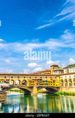 Pont en pierre Ponte Vecchio avec bâtiments colorés maisons sur le bleu de la rivière Arno reflétant l'eau dans le centre historique de Florence, bleu ciel blanc Banque D'Images