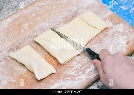 Un homme coupe la pâte en morceaux avec un couteau noir. Couper le panneau de bois avec la pâte. Cuisine de gâteaux faits maison Banque D'Images