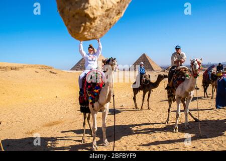 Une adolescente semble détenir un rocher. Une famille manèges chameaux au complexe Giza Pyramid, Giza, Egypte. Banque D'Images