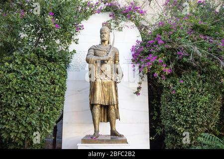 Statue grecque en bronze sur socle dans des buissons et des fleurs vertes Banque D'Images