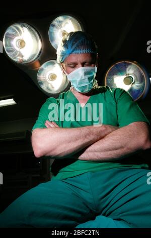 Un chirurgien fatigué est assis sur une table d'opération avec des bras repliés Banque D'Images