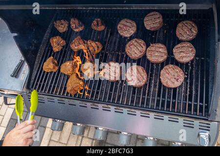 Homme cuisine boeuf hamburgers et côtelettes d'agneau barbecue sur un barbecue au gaz propane extérieur été Banque D'Images