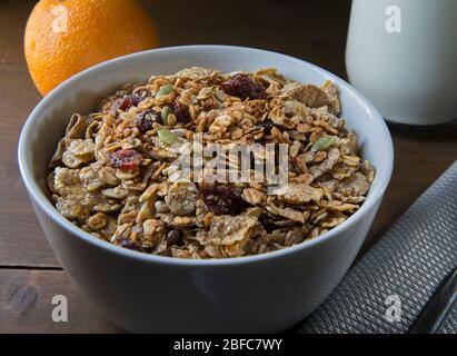 Céréales et granola dans un bol blanc, avec un verre de lait et d'orange sur le côté, sur une table rustique en bois dans le cadre d'un petit-déjeuner Banque D'Images