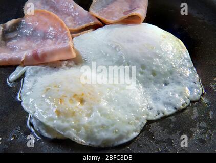 Cuisson frite sur des œufs moyens et des tranches de jambon sur une poêle huileuse, concept de petit déjeuner classique Banque D'Images