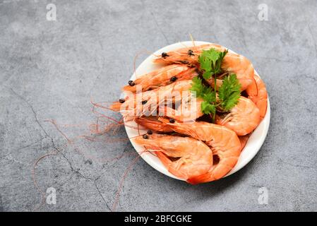 crevettes fraîches sur la plaque blanche avec ingrédients coriandre aux herbes / cuisson des crevettes aux fruits de mer servies sur fond de table gris Banque D'Images