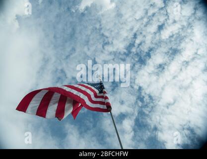 Drapeau américain des États-Unis souffle dans le vent haut sur le flagpole dominant au-dessus de fond de ciel bleu nuageux symbole des étoiles et des rayures de l'amérique Banque D'Images