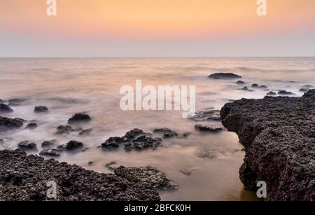 Paysage incroyable de roches ignées côtières avec horizon visible clair pendant le coucher du soleil/lever du soleil. Les vagues de la mer qui écrasent les roches sont lissées par exposition Banque D'Images