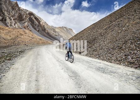 Man on mountain bike rides sur la route dans les hautes montagnes contre fond de ciel bleu.
