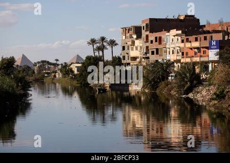 Vue sur un canal près du Caire, Égypte avec les grandes Pyramides de Gizeh en arrière-plan. Banque D'Images