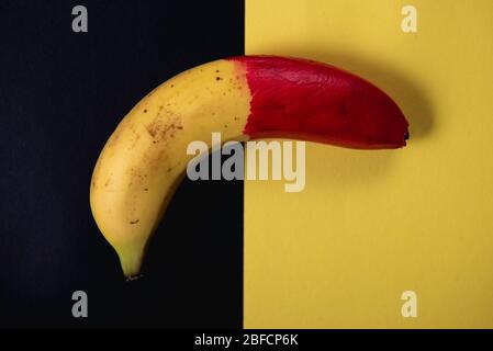 Peau d'un fruit frais de banane peint à moitié en rouge reposant sur un fond noir et jaune. Concept créatif de vie Banque D'Images