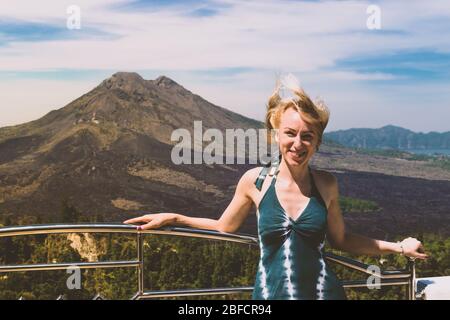 Jeune blonde femme avec robe verte debout devant le volcan du Mont Batur sur l'île de Bali pendant les jours nuageux et venteux Banque D'Images