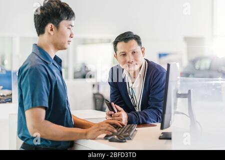 Un mécanicien asiatique saisit le clavier lors de l'entretien du client pour vérifier au centre de maintenance de la salle d'exposition Banque D'Images