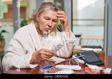 Portrait d'une femme atteinte de maturité et troublée assise à la maison et listant la description des médicaments dans sa main Banque D'Images