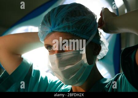 Une chirurgien féminin lie son masque chirurgical autour de son visage sous les lumières du théâtre Banque D'Images