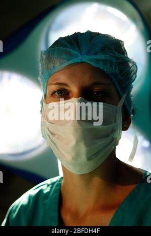 Un chirurgien féminin regarde directement la caméra de dessous les lumières chirurgicales Banque D'Images