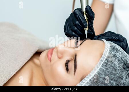 Les mains de professionnels du cosmologiste font le maquillage permanent sur les sourcils de la jeune femme, près. Banque D'Images