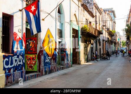 La Havane, Cuba - 25 juillet 2018 : la vieille rue de la Havane avec des graffitis peints sur des bâtiments, un drapeau cubain accroché et des gens qui vont sur leur journée nomale. Banque D'Images