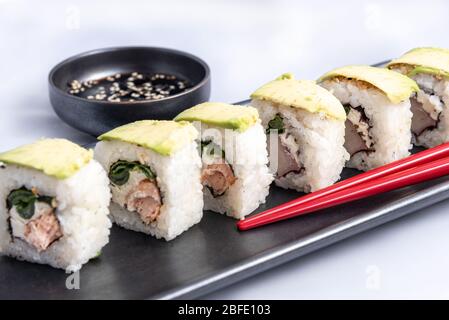 Rouleau de sushi avec wrap avocat, saumon grillé, fromage de philadelphie et oignons verts réservoir noir et baguettes rouges. Banque D'Images