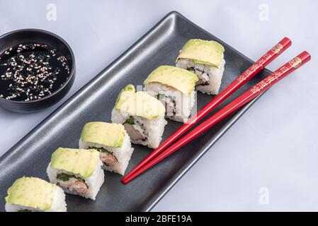 Rouleau de sushi avec wrap avocat, saumon grillé, fromage de philadelphie et oignons verts réservoir noir et baguettes rouges. Banque D'Images