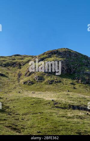 Vue sur le visage regardant une colline rocheuse écossaise verte avec ciel bleu clair sans nuages au-dessus Banque D'Images