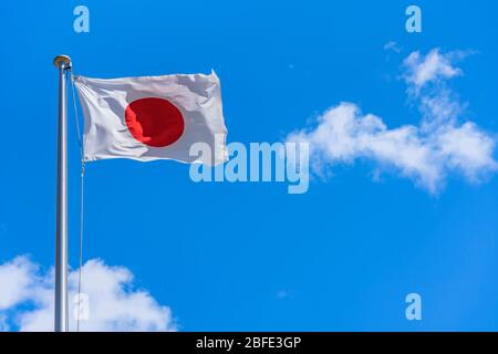 Drapeau national japonais se fouitant au vent contre un ciel bleu ensoleillé. Banque D'Images