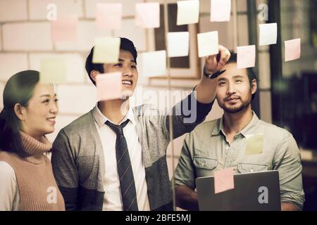 trois jeunes entrepreneurs asiatiques de petite entreprise se moquant de leurs discussions au bureau à l'aide de notes collantes Banque D'Images