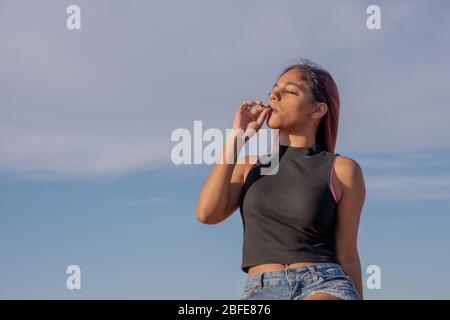 Port Elizabeth, Afrique du Sud avril 2020 Jeune femme fumant de la marijuana contre le ciel bleu clair Banque D'Images