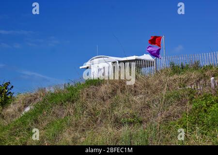 Support de sauveteur avec drapeaux d'avertissement montrant un danger de vie marine dangereuse et un danger de surf, sur le point élevé de dune de sable, et de clôtures de sable. Banque D'Images