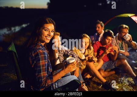 Fille avec une tasse de thé dans le cadre d'amis par le feu dans la nuit Banque D'Images