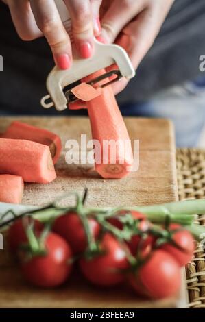 Peler les carottes de près. Girly mains préparer la nourriture dans la cuisine. Banque D'Images