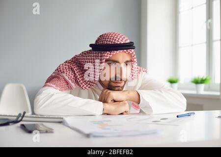 Homme arabe calme regardant assis sur une table dans une salle de bureau Banque D'Images