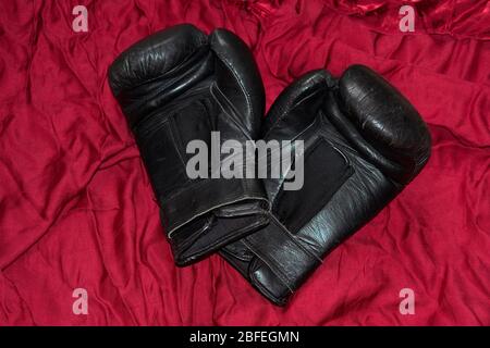 Une paire de gants de boxe en cuir noir que je menais sur satin rouge. Banque D'Images
