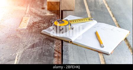 dessiner des produits en bois préparés dans un cahier de travail dans une menuiserie. mètre à ruban, crayon et carnet sur la table avec tronçonneuse Banque D'Images