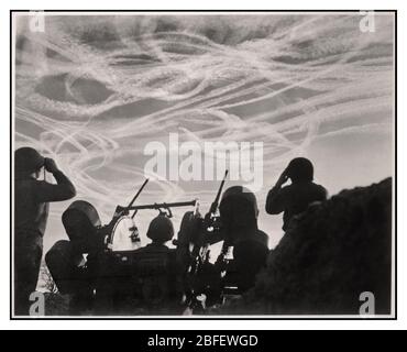 Vintage 1940 de LA BATAILLE DE LA BOSSE de chien aérien combat Vapor Trails au-dessus de l'Allemagne image de la Seconde Guerre mondiale de GIS d'un M-51 anti-Aircraft batterie regardant le combat aérien, silhoueted contre le ciel allemand strié avec des sentiers de vapeur de combat de dogfight des avions alliés et ennemis, engagés dans le combat de chien de Noël. Près de Puffendorf, Allemagne. Les combats de chiens du jour de Noël ont parsemé le ciel de pistes de vapeur des avions alliés et allemands. Les soldats d'une batterie antiaérienne regardent l'action au-dessus de Puffendorf, Allemagne. 25 décembre 1944. Bataille des Bulge, Guerre mondiale 2. Banque D'Images