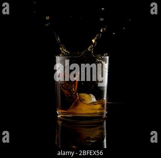 Plongez dans un verre de whisky et de bloc de glace tombant sur fond noir Banque D'Images