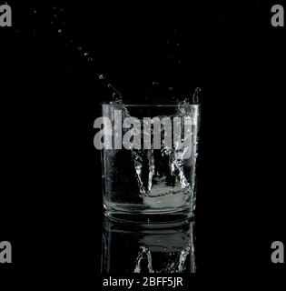 presque noir et blanc d'une éclaboussure d'un cube de glace tombant dans un verre d'eau Banque D'Images