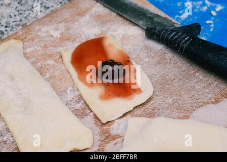 Fabrication de petits pains avec confiture de fraises. Cuisson maison. Une planche en bois saupoudrée de farine et un couteau avec poignée noire Banque D'Images