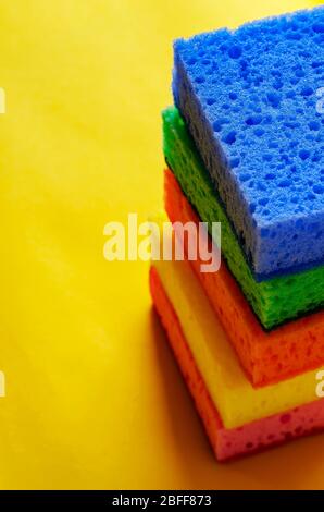 Éponges poreuses de cuisine. Une pile d'éponges de cuisine multicolores sur fond jaune. Un jeu de nouveaux accessoires lumineux pour le nettoyage. clea commercial Banque D'Images