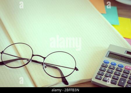 Un bloc-notes ouvert avec de l'espace pour le texte. Lunettes à l'ancienne, calculatrice, notes adhésives colorées, style vintage, concept de bureau Banque D'Images
