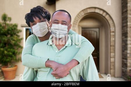 Couple afro-américain affectueux portant des masques de visage médical devant la maison. Banque D'Images